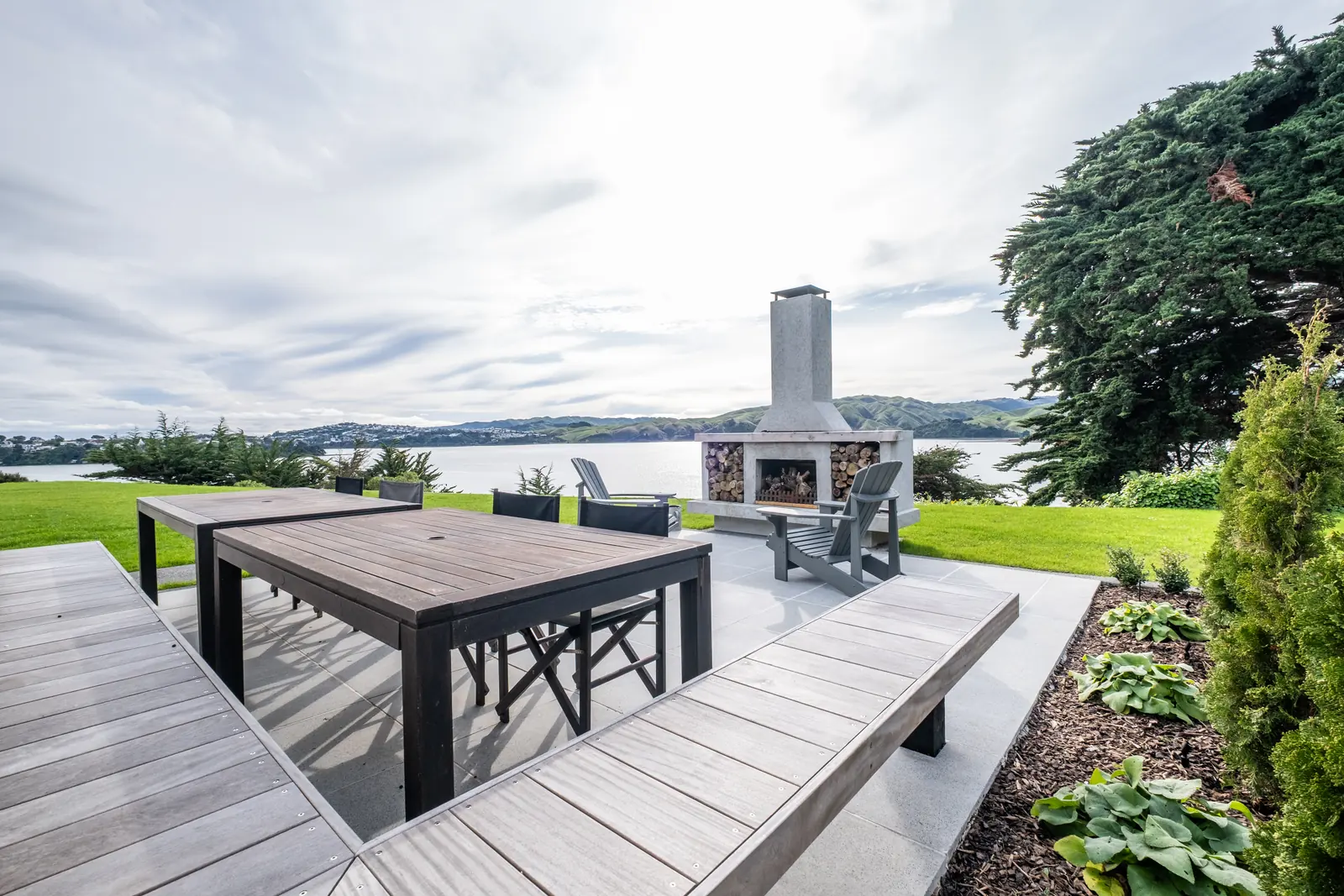 Paved dining terrace with benches and an outdoor fireplace above the harbour at Paremata, built by Distinctive Landscapes