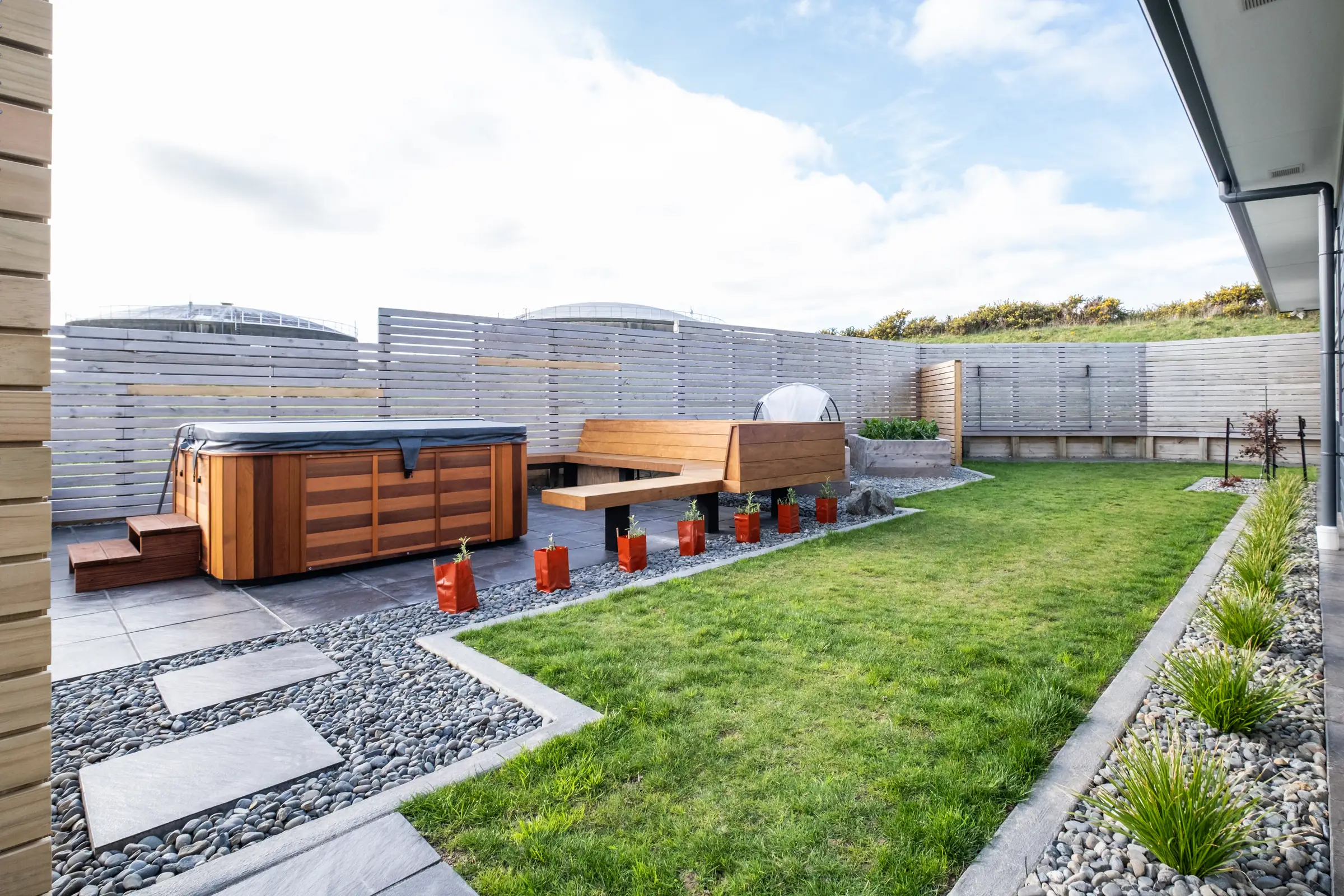 Rotorua Grove - A bare new-build section turned into a sheltered courtyard: paving, built-in seating, a spa pool surround, timber screens and raised veggie beds.